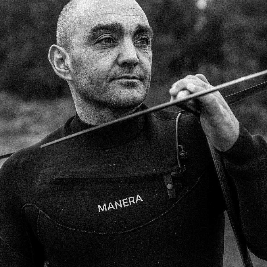 Portrait eines Surfers der ein Foill auf der Schulter trägt.